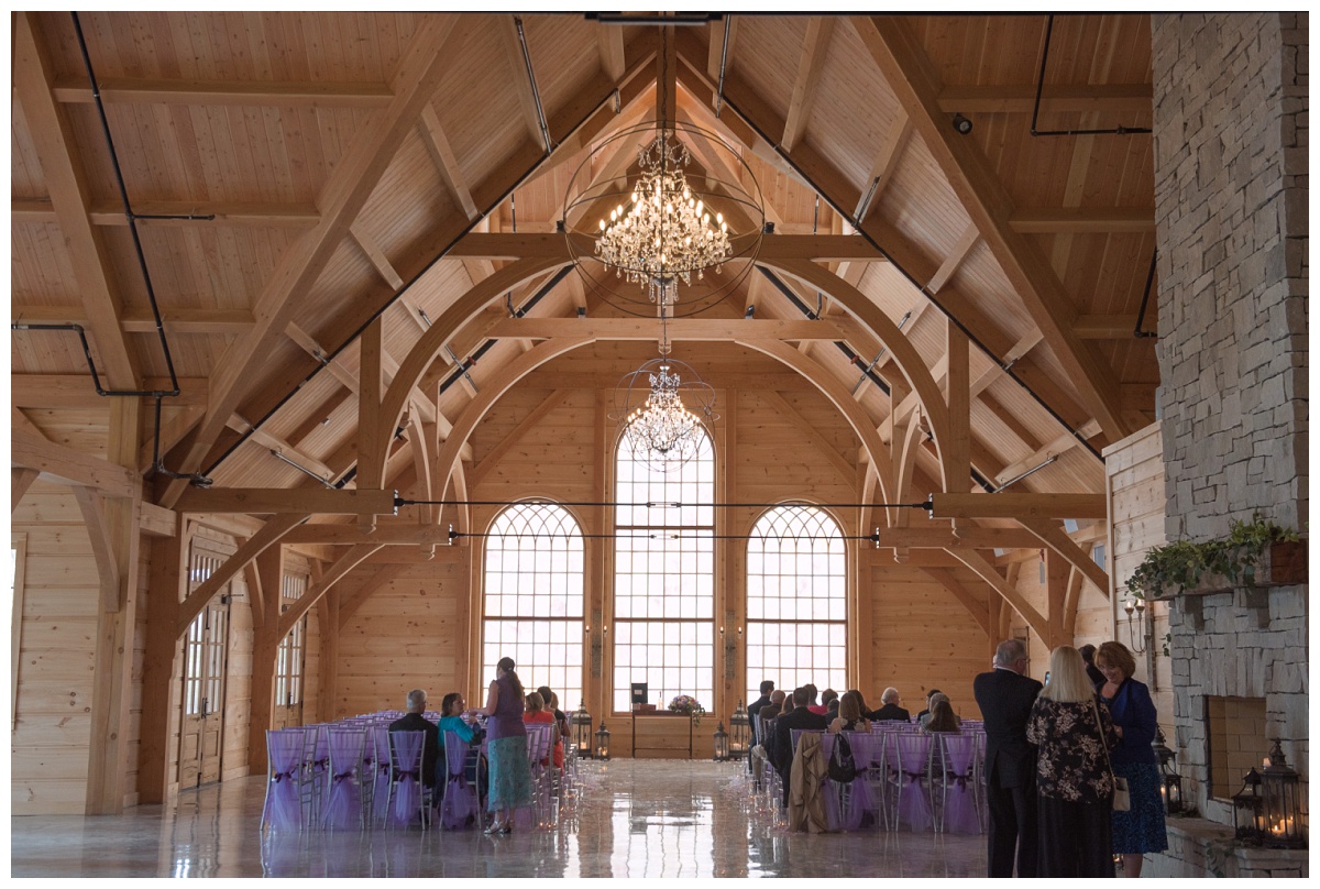 Vaulted cedar cathedral ceiling with crystal and iron chandeliers, back wall accented with three arched windows with cream and lilac stained glass at Stone House of St. Charles, a St Louis wedding venue
