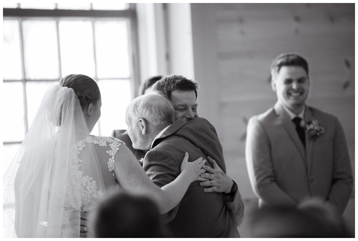 black and white image of groom embracing bride's father during wedding ceremony